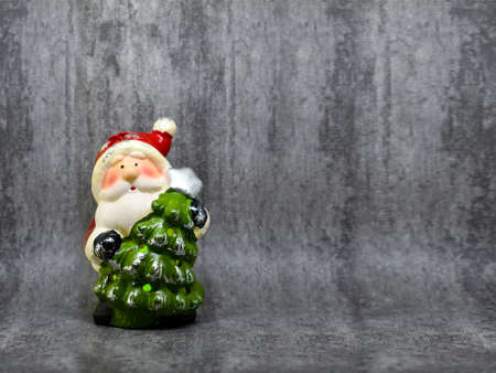 Statuette of Santa Claus with a Christmas tree on a gray background with space for text. Christmas greeting card. Christmas decoration. Christmas seasons celebration conceptの写真素材