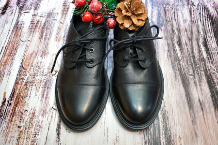 Black leather shoes and Christmas decor on wooden background. Pair of stylish women's boots and spruce twig with Christmas toys on the laminate floor. Leather shoe care, custom tailoring, shoe repairの写真素材