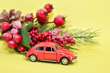 Miniature red car and New Year's decor. Red retro car next to a fir branch on a yellow background. Postcard for the new year, christmas. Place for text.の写真素材