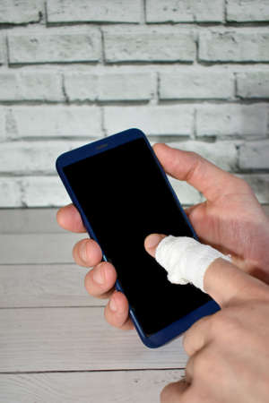 mans hand with bandaged finger holds smartphone to call an ambulance. Accident at work. Close-up Smartphone in hand. call for help, health insurance. mobile app conceptの写真素材