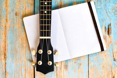 ukulele fretboard and notepad on wooden table, space for text. Home independent online learning to play hawaiian guitar. ukulele on textured wooden background next to notebook. selective focusの写真素材