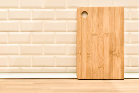 Bamboo wooden chopping board against white brick wall and kitchen countertop background. Light...