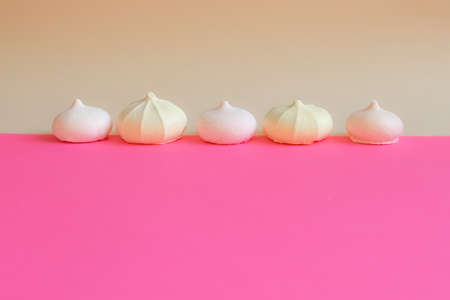 meringue in row. Small cakes meringue on bright pink background. Space for text. Delicate background with sweets. postcard with Light and airy dessert.の写真素材