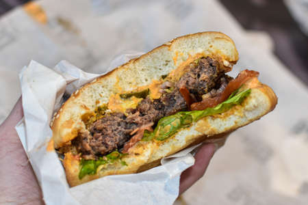 delicious juicy burger in hands of man. Male hands holding hamburger, close-up. Fast food, Unhealthy food. man eating delicious cheeseburger at home. Food delivery.の写真素材