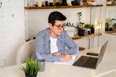 Woman entrepreneur with short black hair with glasses works on laptop in stylish interior of office....