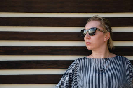 Portrait of a blonde with glasses. Woman looks into the distance, standing against the background of the wall. space for textの写真素材