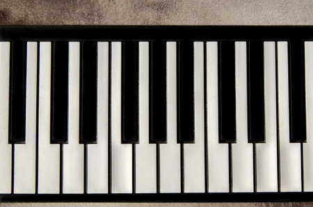 Close-up of a flat piano keyboard, top view. Piano keys on a textured concrete background. Space for text, copy spaceの写真素材