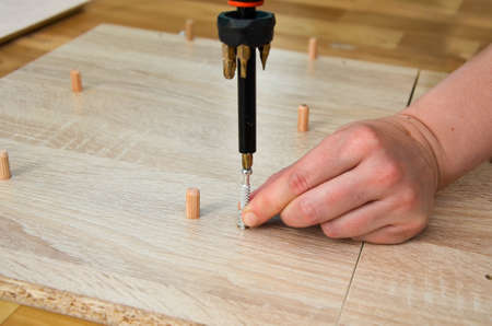 close-up of female hands screwing a metal furniture screw with a screwdriver. The woman collects furniture in the apartment on her own. Furniture assembly, Housework, DIY.の写真素材