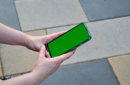 hands hold a smartphone with a chroma key screen. A woman sits on a bench, holds a mobile phone and moves the screen with her finger. The display is made in a color key to replace the informationの写真素材