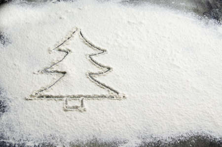 Drawn Christmas tree on flour scattered on the table. Silhouette of a Christmas tree made of flour on a dark concrete background of the kitchen table top. Holiday preparation concept, new year treatsの写真素材