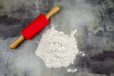 A pile of sifted flour and a rolling pin for rolling out the dough on a dark background of a concrete table top. Sprinkled flour on a cutting board. Space for text. Grainy surface, selective focus.の写真素材