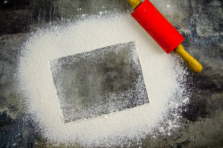 rolling pin and scattered flour in the form of a frame on a dark concrete background of the kitchen...