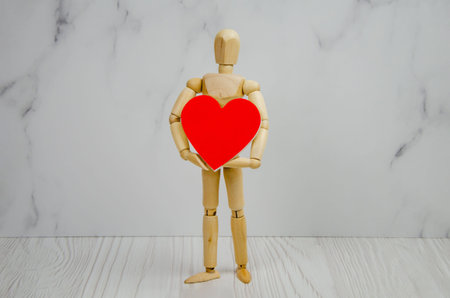 wooden figurine of a man with a big red heart in his hands. the concept of love, friendship, heart health. man holding a heart in his hands, Valentine card. space for text.の写真素材