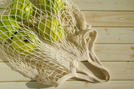 fresh fruits in a mesh bag. Top view, apples in a string bag on a wooden background. Healthy nutrition, vitamins, conscious consumption. space for textの写真素材