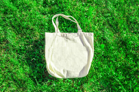 Beige cotton shopping bag on a background of green grass. Zero waste, no plastic, eco-friendly waste recycling concept. Empty layout, template with space for text, logo. Flat layout, copy spaceの写真素材