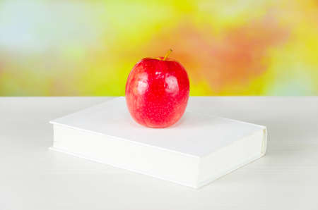white book with juicy fresh apple on desktop over blurry autumn background. schoolbook with red apple. background for school design. back to school.の写真素材