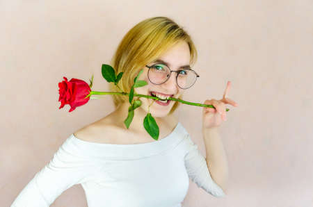 Attractive young woman in playful pose smiling while holding red rose in her teeth. Flirtingの写真素材