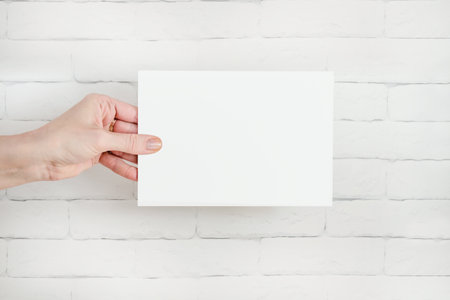 hand holds white blank form against brick wall. Copy space, text space. Layout template, informationの写真素材