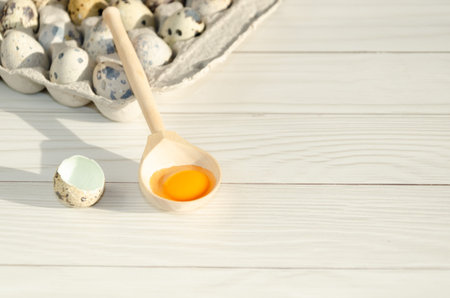 broken quail egg with a bright orange yolk in a wooden spoon among whole quail eggs stacked in a cardboard tray and lying on the table. Space for textの写真素材