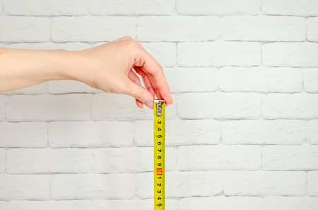 Construction tape measure in a women's hands on background a brick wall. Woman demonstrating wall...