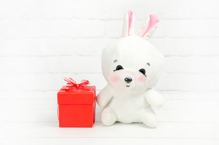 Cute toy white bunny and a red gift box on a light background. Concept for celebrating new year, christmas, valentine's day, birthday. Space for textの写真素材