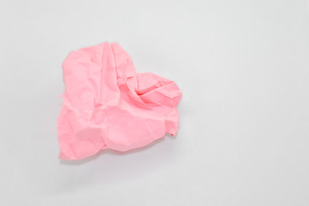 Crumpled pink paper in the shape of a heart on a white background. Space for text. A valentine, a declaration of love, a postcard.の写真素材
