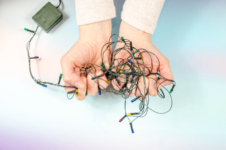 Woman's hands hold tangled Christmas tree garland. Stress before celebration. old tree decorationsの写真素材