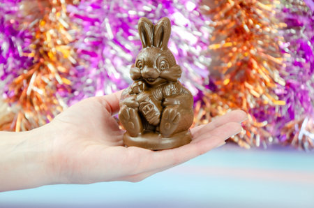 hand holds cute chocolate bunny on shiny background of multi-colored tinsel. chocolate bunny in handの写真素材