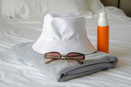 Preparing to visit the beach. There is a towel, panama hat, sunglasses and sun spray on the bed. sun protection. high UV safety and care productsの写真素材