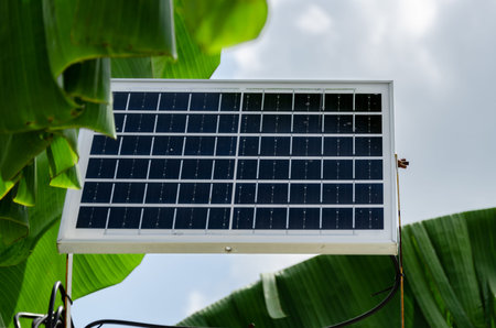 Mini solar battery panel outside. Background of blue sky and banana tree leaves. Concept: the use of...