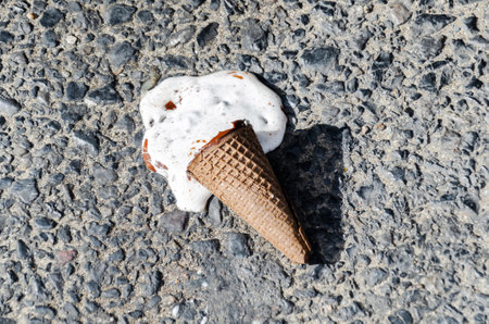 melted ice cream on the sidewalk on a hot summer day. ice cream in a chocolate cone fell to the ground and melted. selective focus.の写真素材