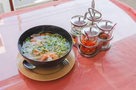 cup of traditional Thai soup with noodles and seafood and spicy spices stand on table in street cafe