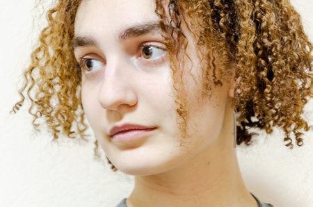 close-up photo of a young attractive woman, short blonde hair with curls. curl curlers. Portrait of a cute, funny curly-haired girl on a beige backgroundの写真素材