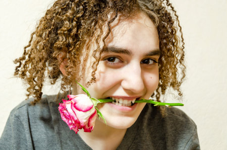 cute curly girl smiles, holding a rose in her teeth. Young woman with a rose. flirting, valentine's day, congratulationsの写真素材