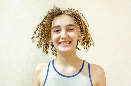 Portrait of a cute, funny curly girl. Headshot of a laughing cheerful young woman with a curly hairstyle on a beige background. naturalness, simplicityの写真素材