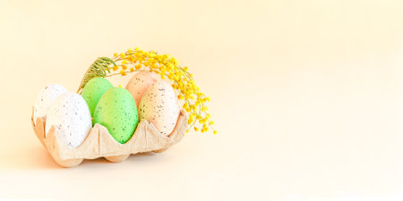 colorful Easter eggs in ecological packaging and a mimosa flower on a pale beige background. Happy Easter. Easter card with space for textの写真素材