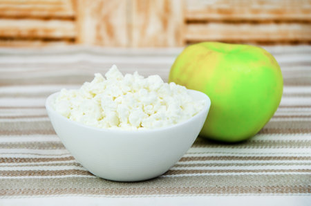 cup of cottage cheese and a fresh apple on a striped cotton tablecloth. Healthy diet food, breakfastの写真素材