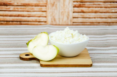 cup of cottage cheese and a fresh apple on a striped cotton tablecloth. Healthy diet food, breakfastの写真素材