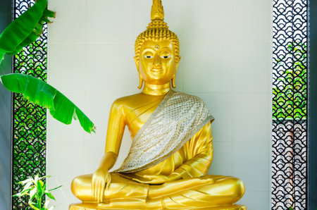 Beautiful Golden Buddha statue in the courtyard against the backdrop of green tropical foliage. Quiet secluded place for prayer and offering. Buddhist altarの写真素材