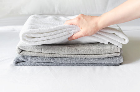 woman puts fresh clean towels on the bed in a hotel guest room, close-up. Woman's hand touches soft terry towels after cleaning the roomの写真素材