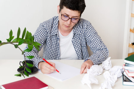 A middle-aged woman sitting at a table in the office holds documents in her hand. woman makes notes,...