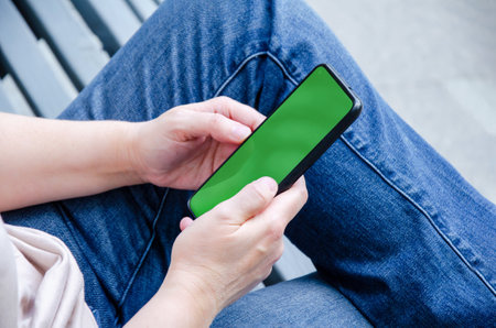 Female hands hold a mobile phone Mockup image, top view. chromakey. Smartphone with green screen. A woman is resting on a park bench with a smartphone.の写真素材