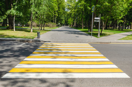 Empty pedestrian crossing across road. Yellow white stripes. Crossing on street for traffic safetyの写真素材