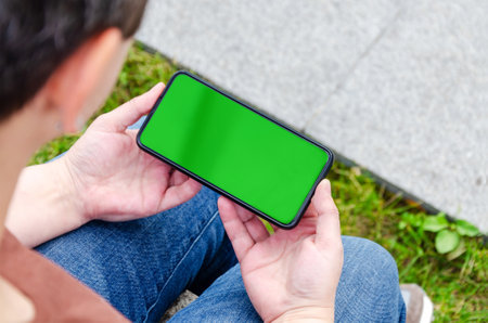 female hands hold a smartphone. Green screen, copy space and chroma key on smartphone screen. Template for inserting an image.の写真素材