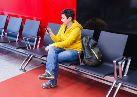 traveler woman with black short hair uses her mobile phone to read and send messages while sitting in an airport terminal waiting for her flight.の写真素材