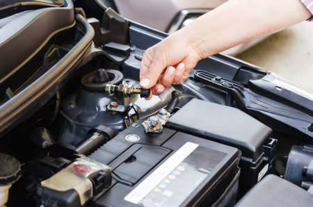 disconnecting the battery in the car before a long parking. A woman disconnects a car battery terminal under an open car engine hood.の写真素材