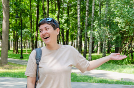 Black-haired woman smiling, greeting waving her hand, meeting acquaintances on a walk in the park. woman greets friends from afar.の写真素材