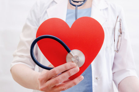 Close-up of female doctors hand holding a large red heart and a stethoscope