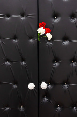 black doors with leather upholstery and a bouquet of four carnations. Mourning, tragic background....