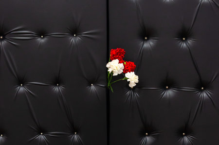 black doors with leather upholstery and a bouquet of four carnations. Mourning, tragic background. Concept of farewell, parting, tragedyの写真素材